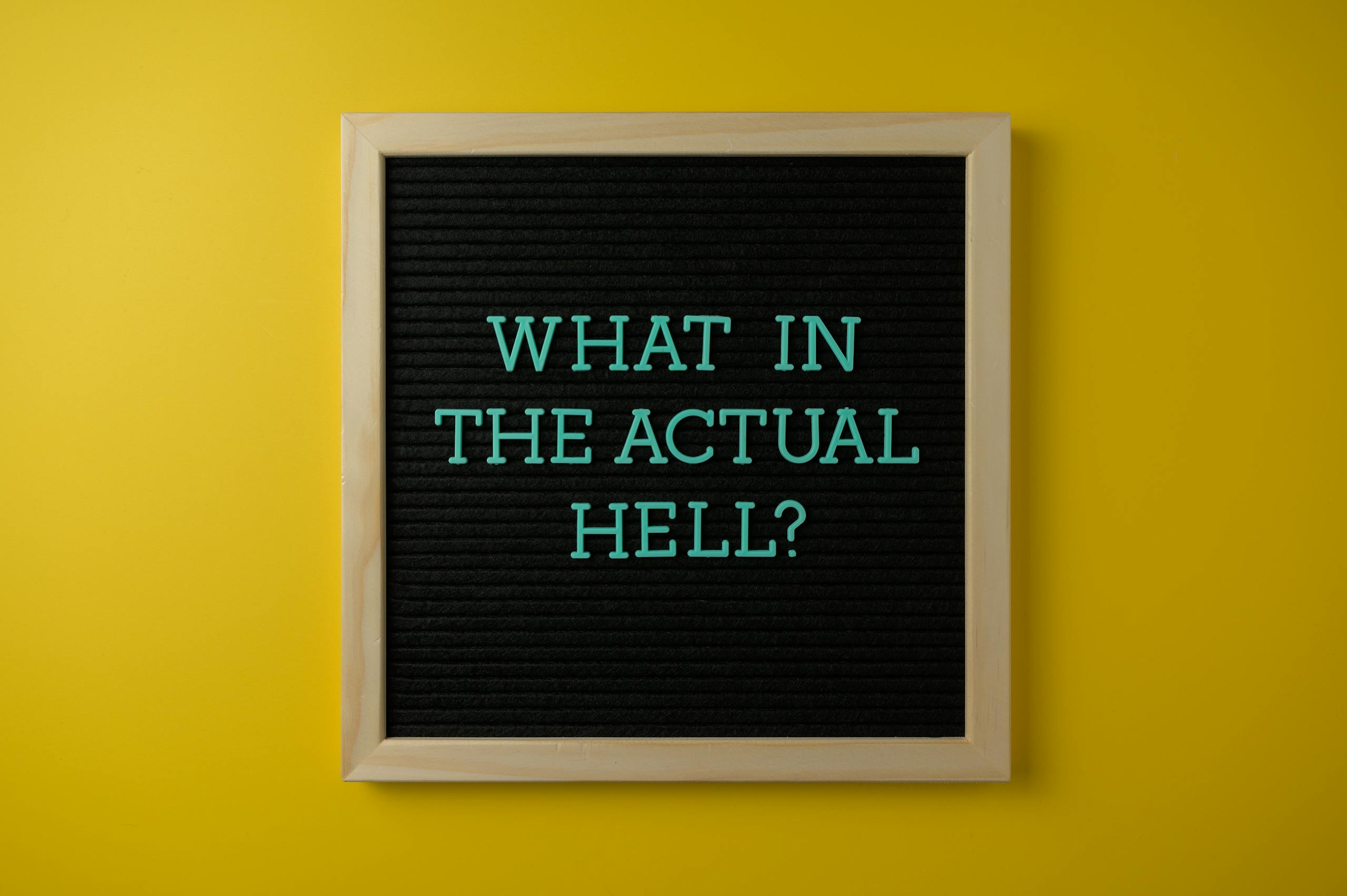 Letter board with humorous quote 'What in the actual hell?' on a vibrant yellow backdrop.